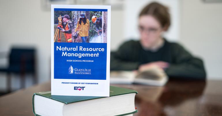 A brochure detailing information about the Glenville State University Natural Resource Management High School Program is featured with a student reading in the background. (GSU Photo/Kristen Cosner)