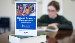 A brochure detailing information about the Glenville State University Natural Resource Management High School Program is featured with a student reading in the background. (GSU Photo/Kristen Cosner)