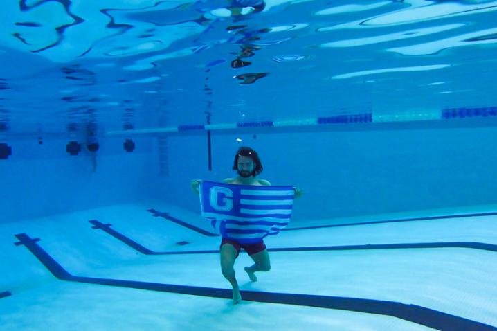 Student under water in a swimming pool holding a Glenville Flag