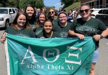 Alpha Theta Xi sisters holding up an ATX Flag