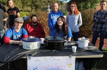 Alpha Psi Omega members sitting at a table with slow cookers