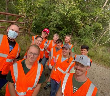 Forestry Club members standing on the edge of woods, smiling and wearing safety vests