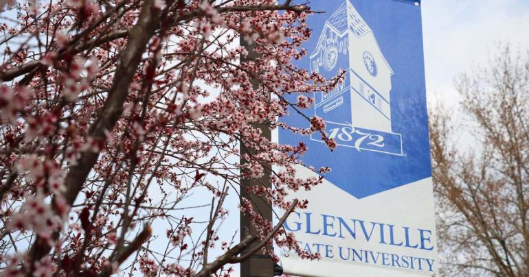 A Glenville State University banner hangs on campus among spring blooms. (GSU Photo/Seth Stover)