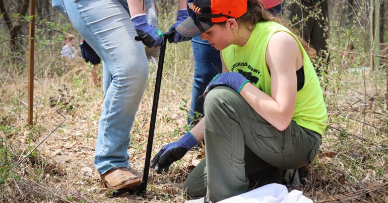 Glenville State University Natural Resource Management student Della Moreland places a sapling in the ground as another student uses a tree-planting bar to create an opening in the soil. (GSU Photo/Seth Stover)