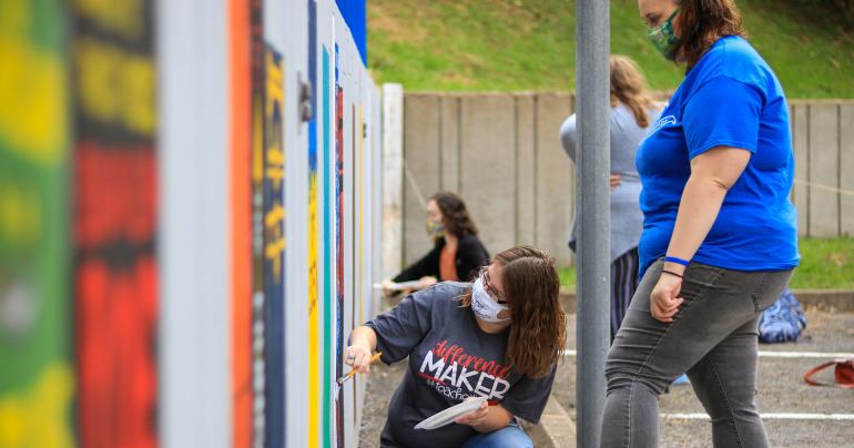 Glenville State College students add to the colorful bookshelf mural behind the Robert F. Kidd Library (GSC Photo/Kristen Cosner)