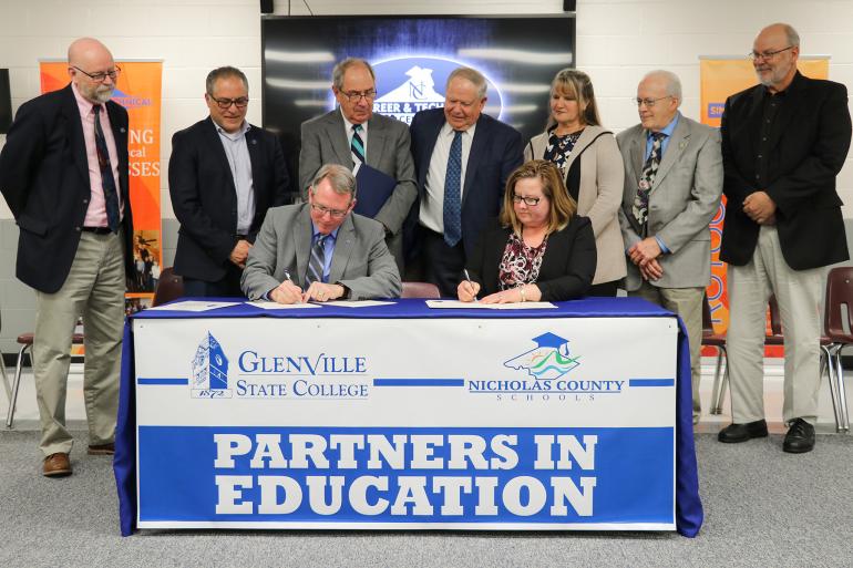 Glenville State College President Dr. Tracy Pellett (seated, left) and Nicholas County Schools Superintendent Dr. Donna Burge-Tetrick (seated, right) sign an agreement backed by GSC representatives, Nicholas County Board of Education members, and Nicholas County and Richwood High School principals