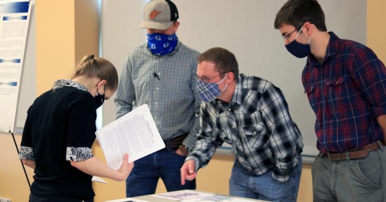 Glenville State College Honors Program students (standing, l-r) Asa Dick, Eli Henthorn, and Jacob Amick explain their Pioneer Showcase entry to an attendee. Their work, a surveying and preservation project on the “Lost Graves of Gilmer County,” tied for first place in the Honors Program Presentations category. (GSC Photo/Dustin Crutchfield)