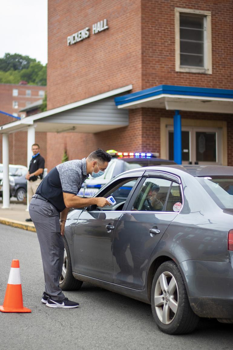 Glenville State College’s Assistant Athletic Director of Athletic Media Relations Jonathan Griffin performs a temperature scan of a commuter entering campus; all vehicles and pedestrians visiting Glenville State are being screened as part of Coronavirus precautions