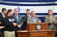 With incoming Glenville State College President Dr. Tracy Pellett at the podium, (l-r) Delegate Roger Hanshaw (R-Clay), GSC student Justin Woods, Board of Governors Chair Greg Smith, Student Government Association President Cameron Woods, and Delegate Brent Boggs (D-Braxton) listen to his announcement on Thursday morning